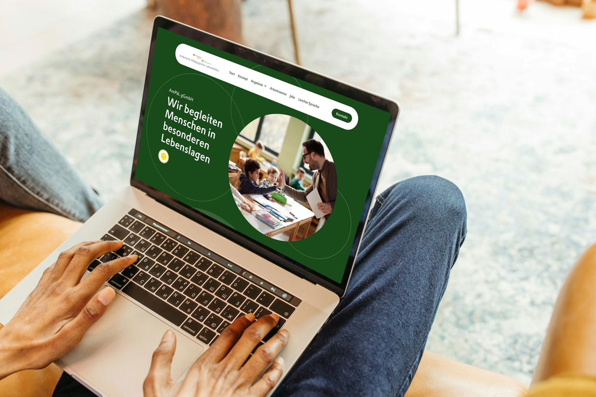 Startseite der barrierefreien Website ampael.de auf einem Laptop. Zu sehen ist ein Mann, der einem Kind im Klassenzimmer die Hand gibt. Webdesign von Grafikstudio Carreira für die Ambulanten Pädagogischen Lebenshilfen (AmPaL).
