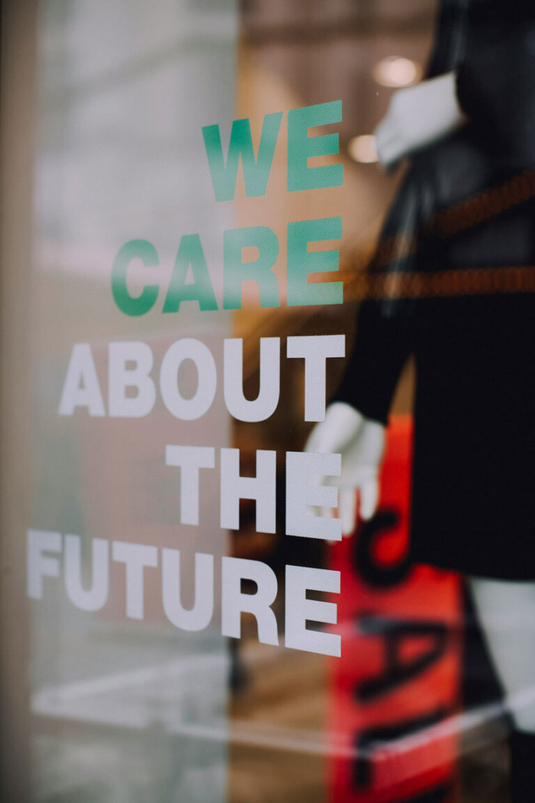 Auf einer Glasscheibe steht in großen Buchstaben „We care about the future“. Im Hintergrund ist unscharf eine Person in formeller Kleidung zu sehen. Das Bild symbolisiert verantwortungsvolles, zukunftsorientiertes Marketing und steht für barrierefreie Kommunikation mit gesellschaftlicher Verantwortung.