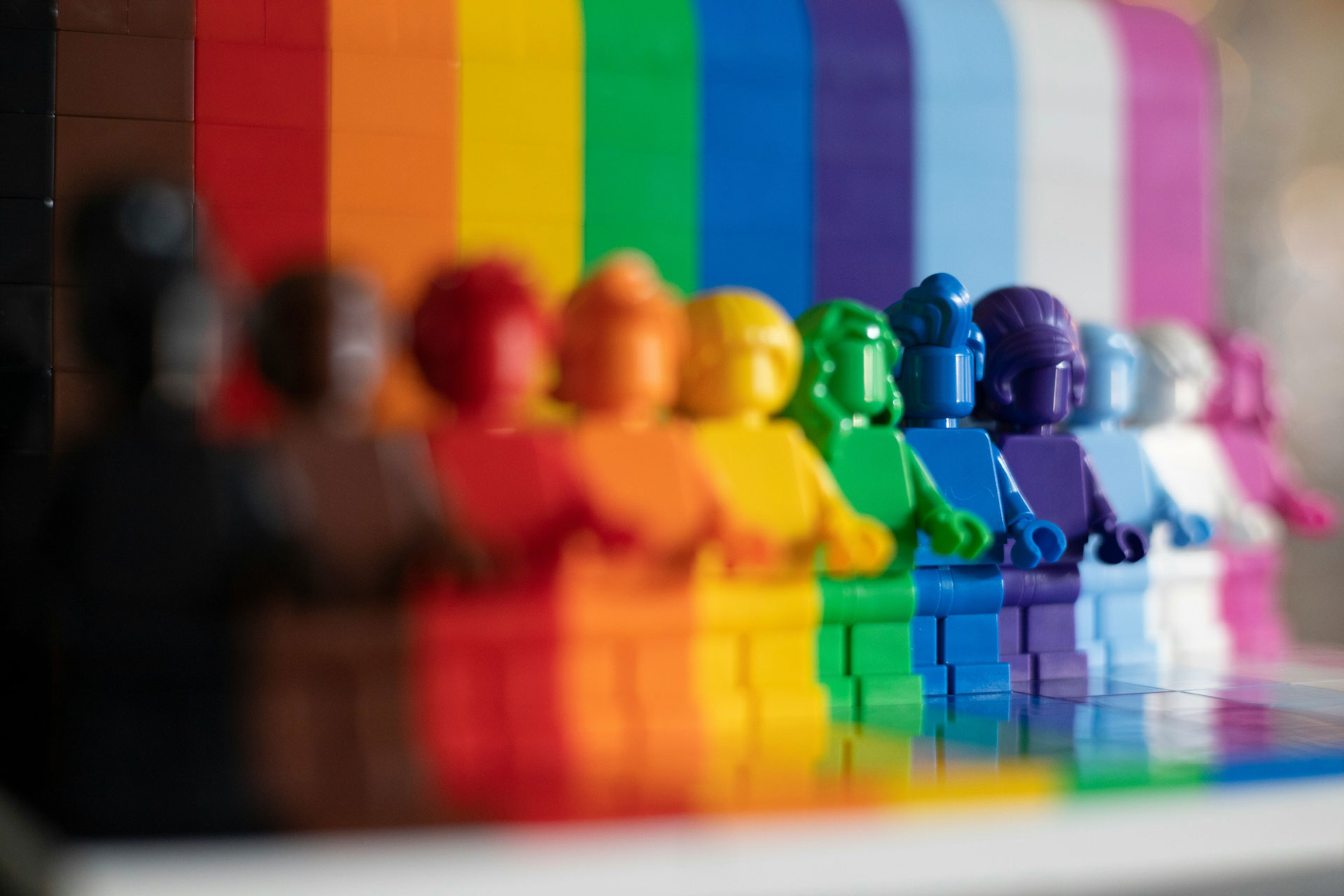 Reihe farbiger LEGO-Figuren vor einem Regenbogenhintergrund als Symbol für Vielfalt, Inklusion und gleichberechtigte Teilhabe im barrierefreien Marketing von Seite an Seite.