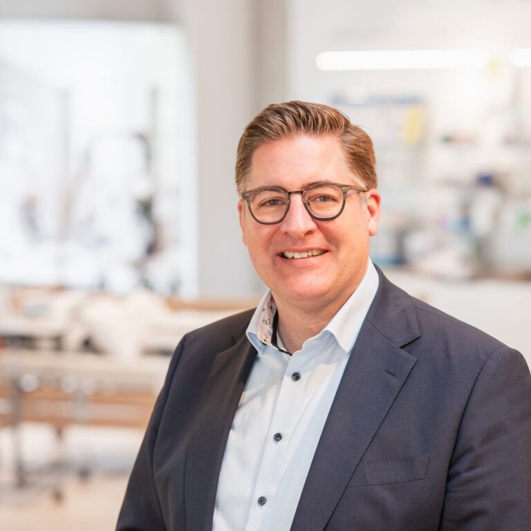 Elmar Bitter, Geschäftsführer von Orthopartner, lächelt in hellen Geschäftsräumen mit orthopädischer Ausstattung im Hintergrund. Anlass ist ein Interview mit Seite an Seite - dem Team für barrierefreies Marketing.